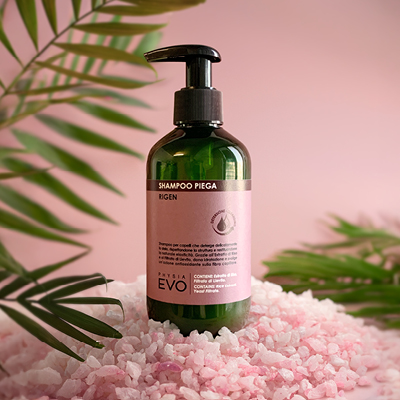 Immagine prodotto Shampoo Piega ambientata  su sfondo rosa decorata con foglie verdi e sale rosa 